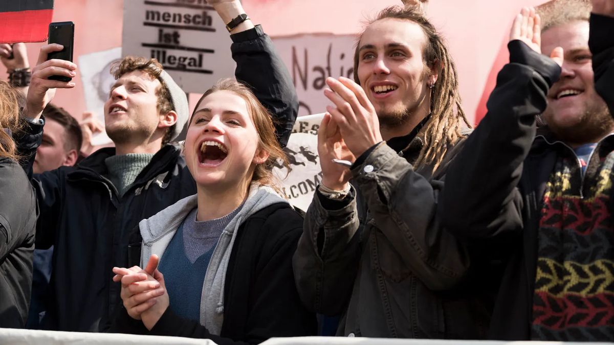 Une foule de jeunes applaudissant et applaudissant lors d'une manifestation dans And Tomorrow the Entire World.