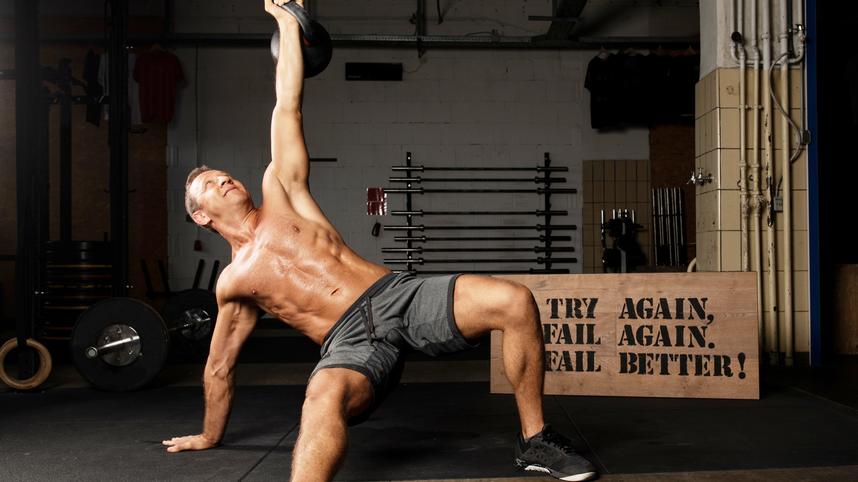 Homme effectuant une préparation turque pendant l'entraînement avec le bras gauche étendu tenant un kettlebell et la jambe gauche pliée et la jambe droite étendue