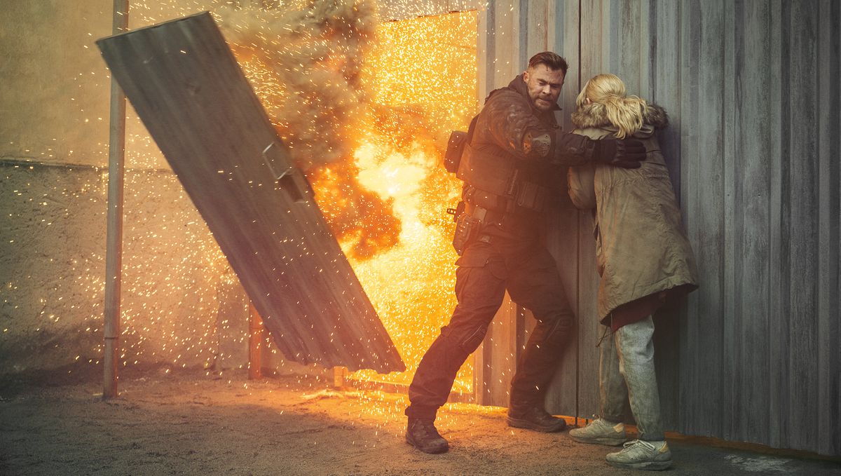 Le mercenaire Tyler Rake (Chris Hemsworth) et sa belle-sœur Ketevan (Tinatin Dalakishvili) s'abritent contre un mur en tôle ondulée alors qu'une porte de ce mur explose dans Extraction 2