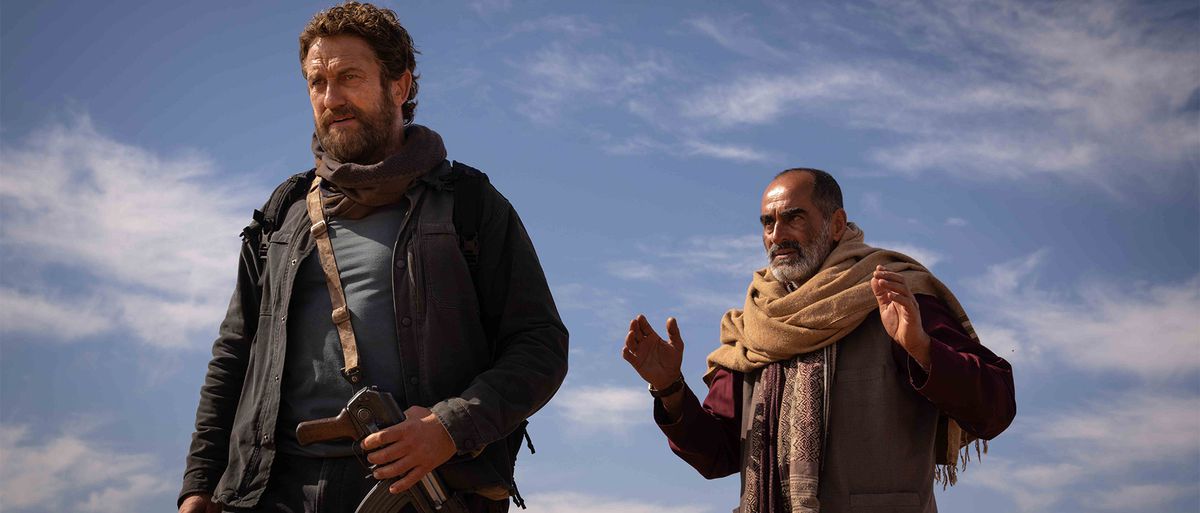 Un Navid Negahban barbu fait des gestes à Gerard Butler avec un ciel bleu derrière eux à Kandahar.