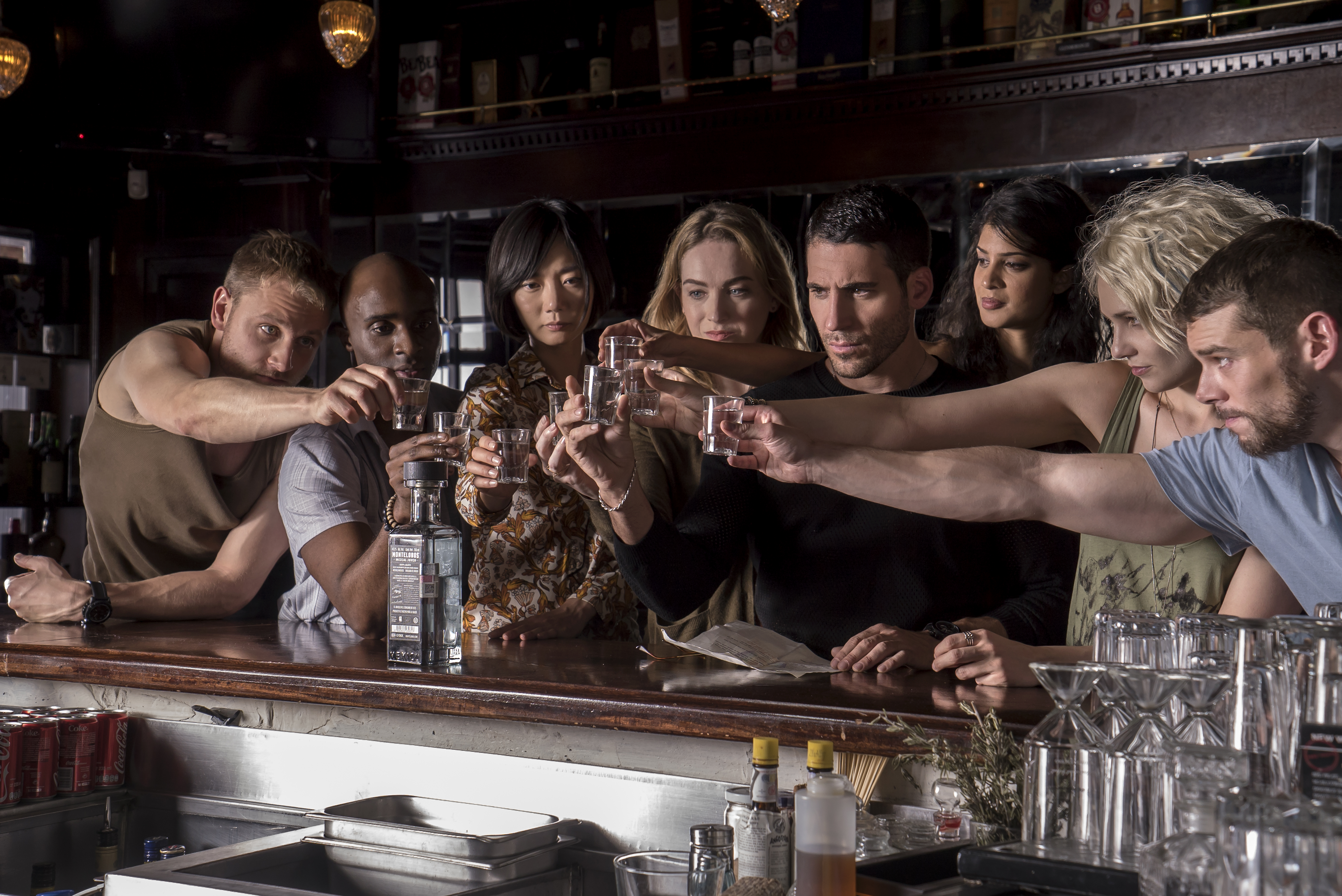 (De gauche à droite) Les personnages Wolfgang (Max Riemelt), Capheus (Toby Onwumere), Sun (Bae Doona), Nomi (Jamie Clayton), Lito (Miguel Angel Silvestre), Kala (Tina Desai), Riley (Tuppence Middleton) , et Will (Brian J Smith) lèvent leurs verres pour porter un toast dans Sense8.