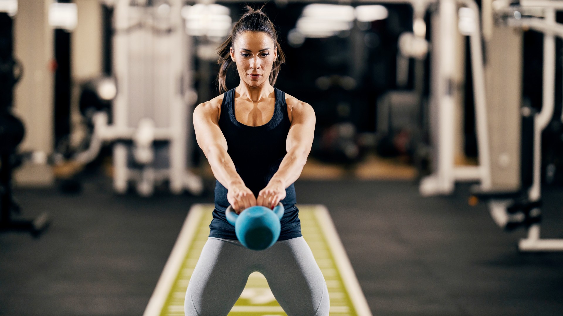 Femme tenant un kettlebell devant elle avec les deux mains alors qu'il se balance devant son corps pendant l'exercice ab