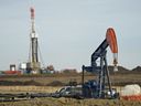 Un pumpjack fonctionne au premier plan avec une plate-forme de forage à l'arrière.