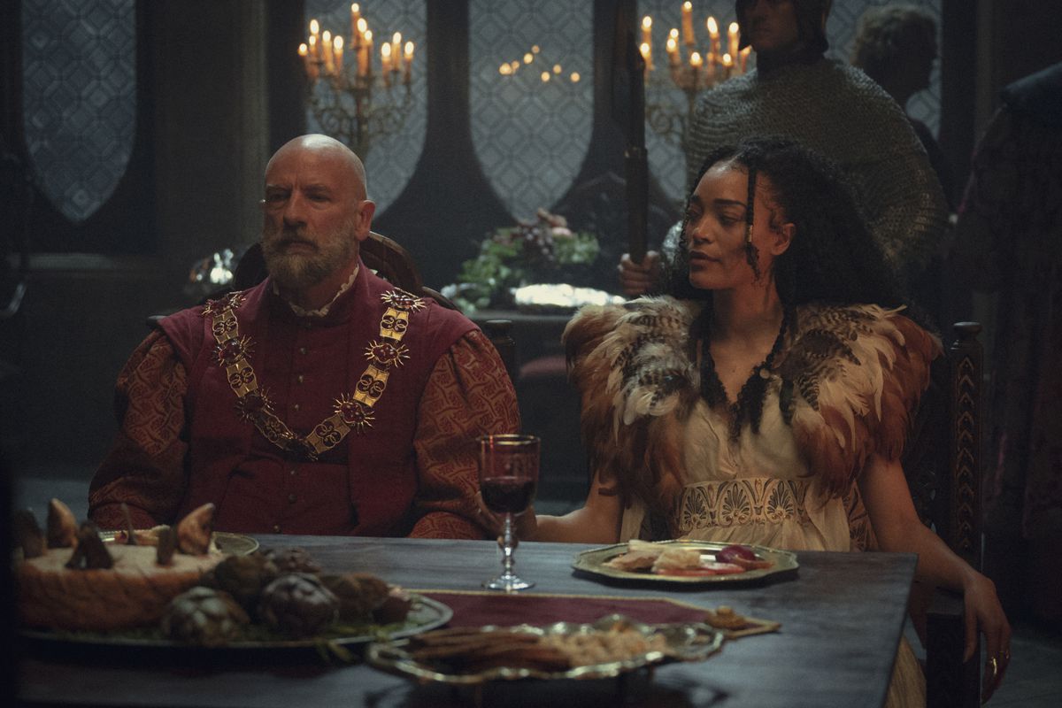 Djikstra et Philippa, deux intrigants, sont assis à une table avec un verre de vin entre eux et une tartinade en son centre dans la saison trois de The Witcher de Netflix