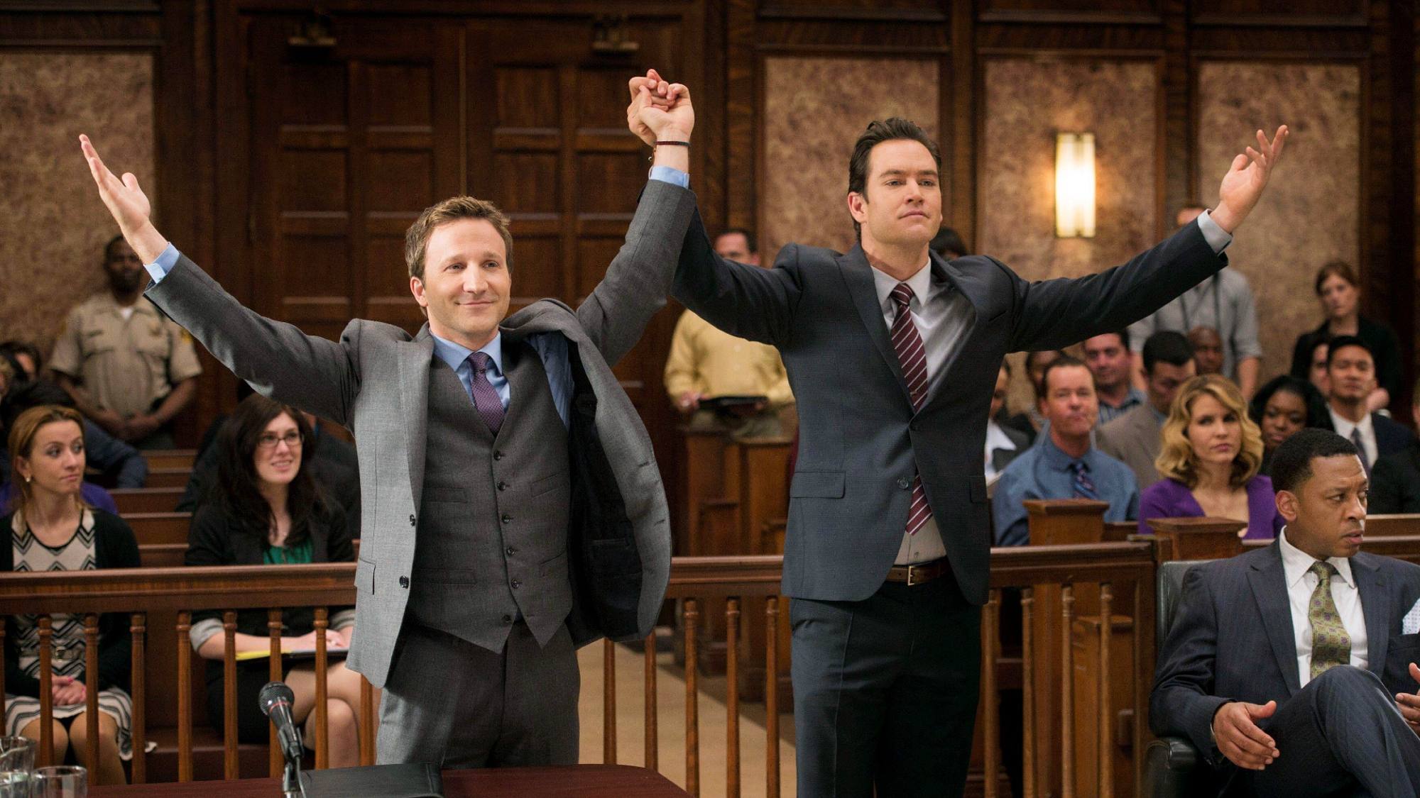 Breckin Meyer et Mark-Paul Gosselaar se tiennent la main dans les airs dans une salle d'audience à Franklin and Bash