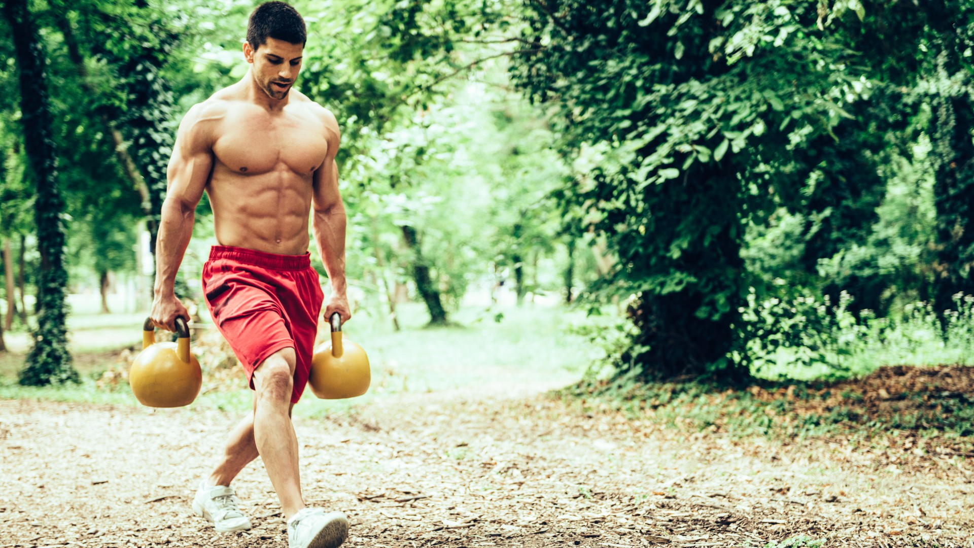 Homme marchant dans un parc tenant deux kettlebells effectuant la marche d'un agriculteur