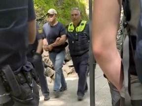 Dans cette image tirée d'une vidéo, un suspect est emmené par deux policiers près du château de Neuschwanstein à Schwangau, dans le sud de l'Allemagne, le jeudi 15 juin 2023. Un Américain a été arrêté après avoir prétendument agressé deux touristes américains près du château de Neuschwanstein dans le sud de l'Allemagne et puis les poussant sur une pente raide, une attaque qui a fait la mort d'une des femmes, ont annoncé jeudi les autorités.