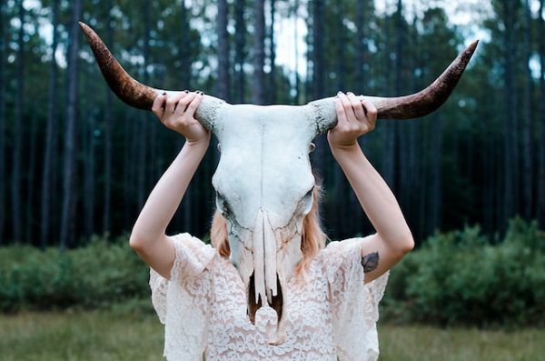 une femme tenant un crâne d'animal portant de la dentelle blanche debout dans un champ ouvert