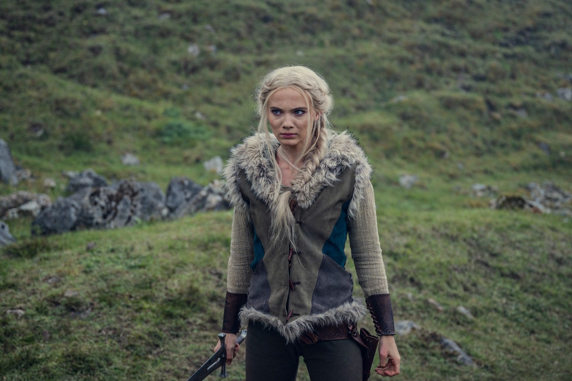 Ciri (Freya Allan) stands with a sword in the open countryside