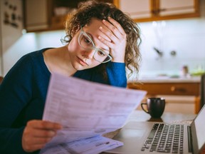 Jeune femme lisant une facture papier, à l'air stressé.