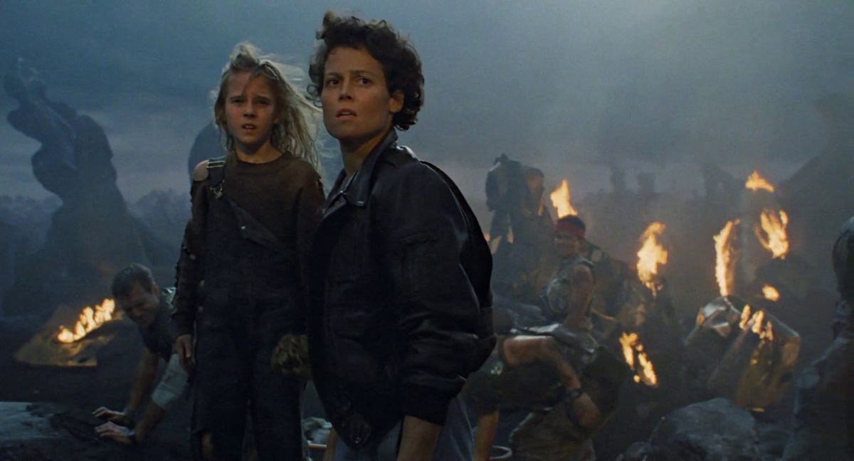 (LR) Carrie Henn et Sigourney Weaver dans le rôle de Newt et Ellen Ripley entourés d'épaves, d'incendies et de marines coloniaux blessés dans Aliens.