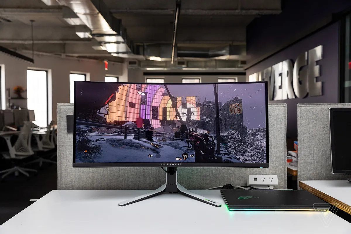 Une image du moniteur de jeu incurvé Alienware AW3423DW sur un bureau blanc, connecté à un ordinateur portable de jeu.