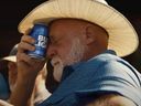 Homme au chapeau de cow-boy tenant une canette Bud Light sur le front.