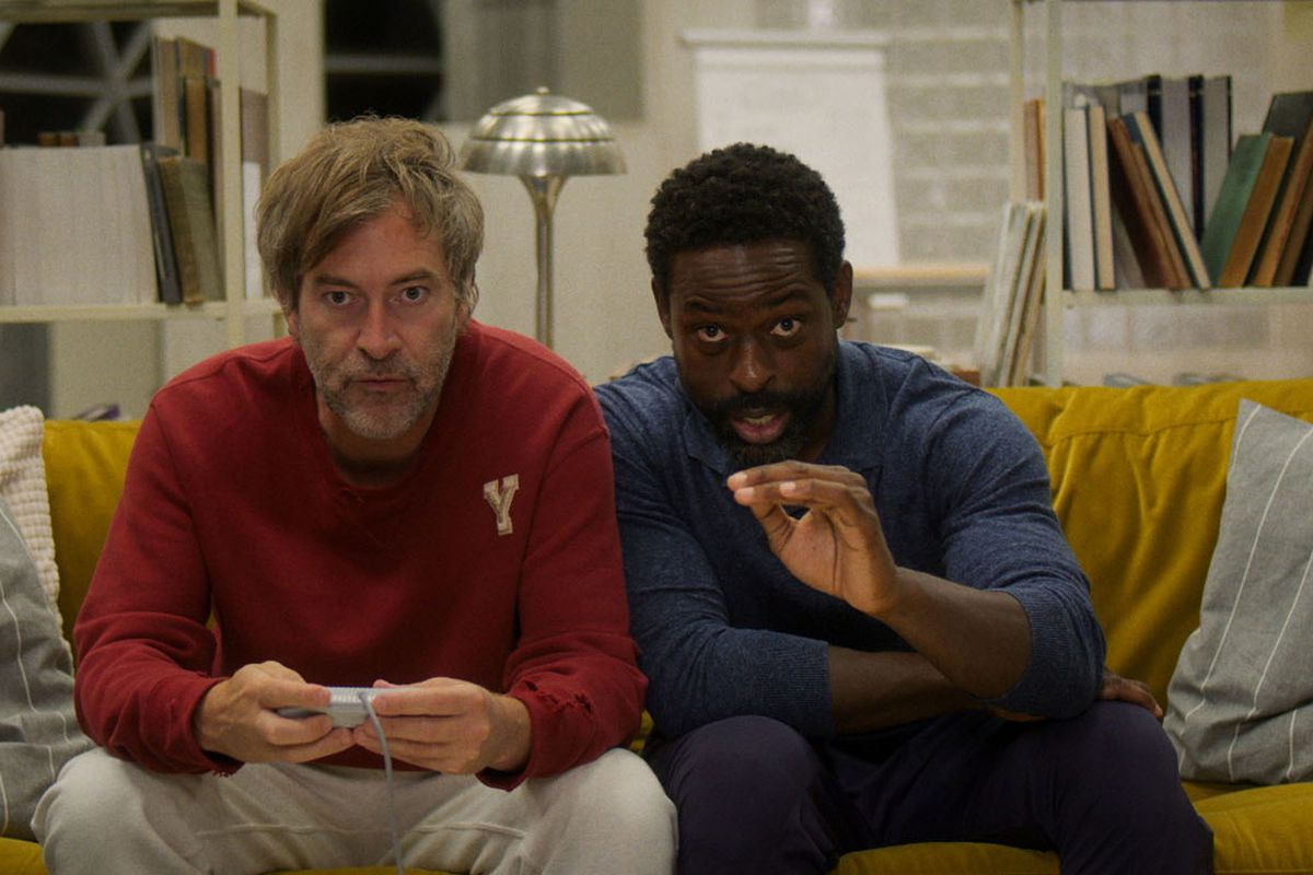 (LR) Mark Duplass et Sterling K. Brown assis sur un canapé et jouant à un jeu vidéo dans Biosphere.