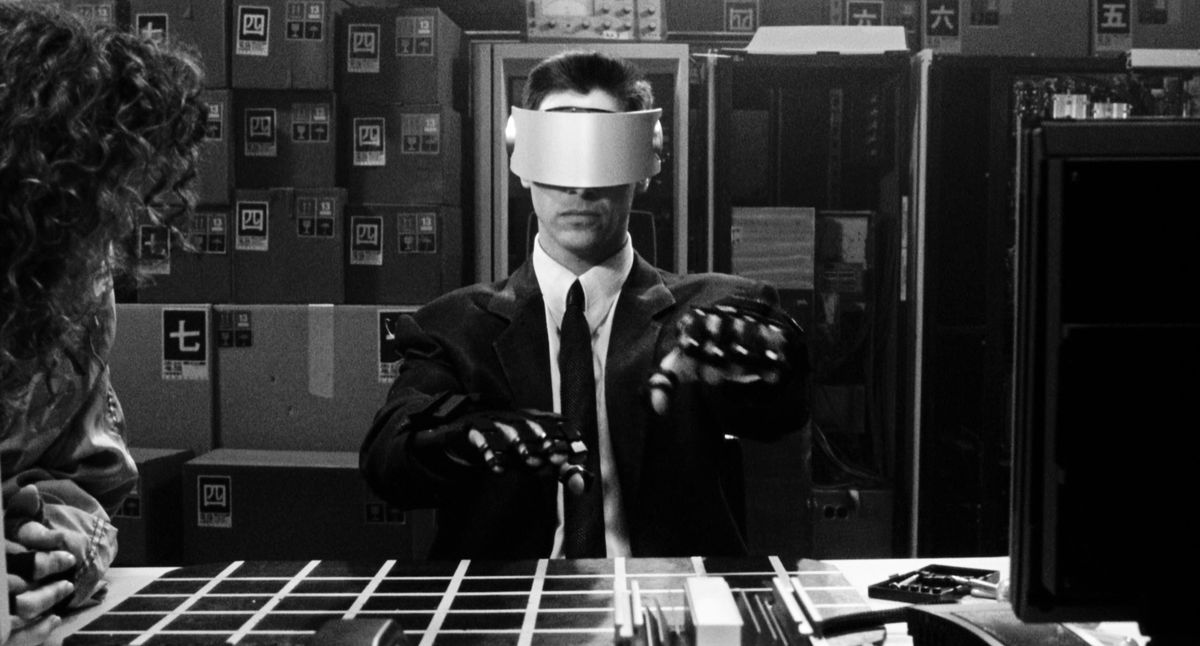 Keanu Reeves dans le rôle de Johnny Mnemonic portant un casque VR et des gants tendant les mains vers l'avant dans Johnny Mnemonic: In Black and White.