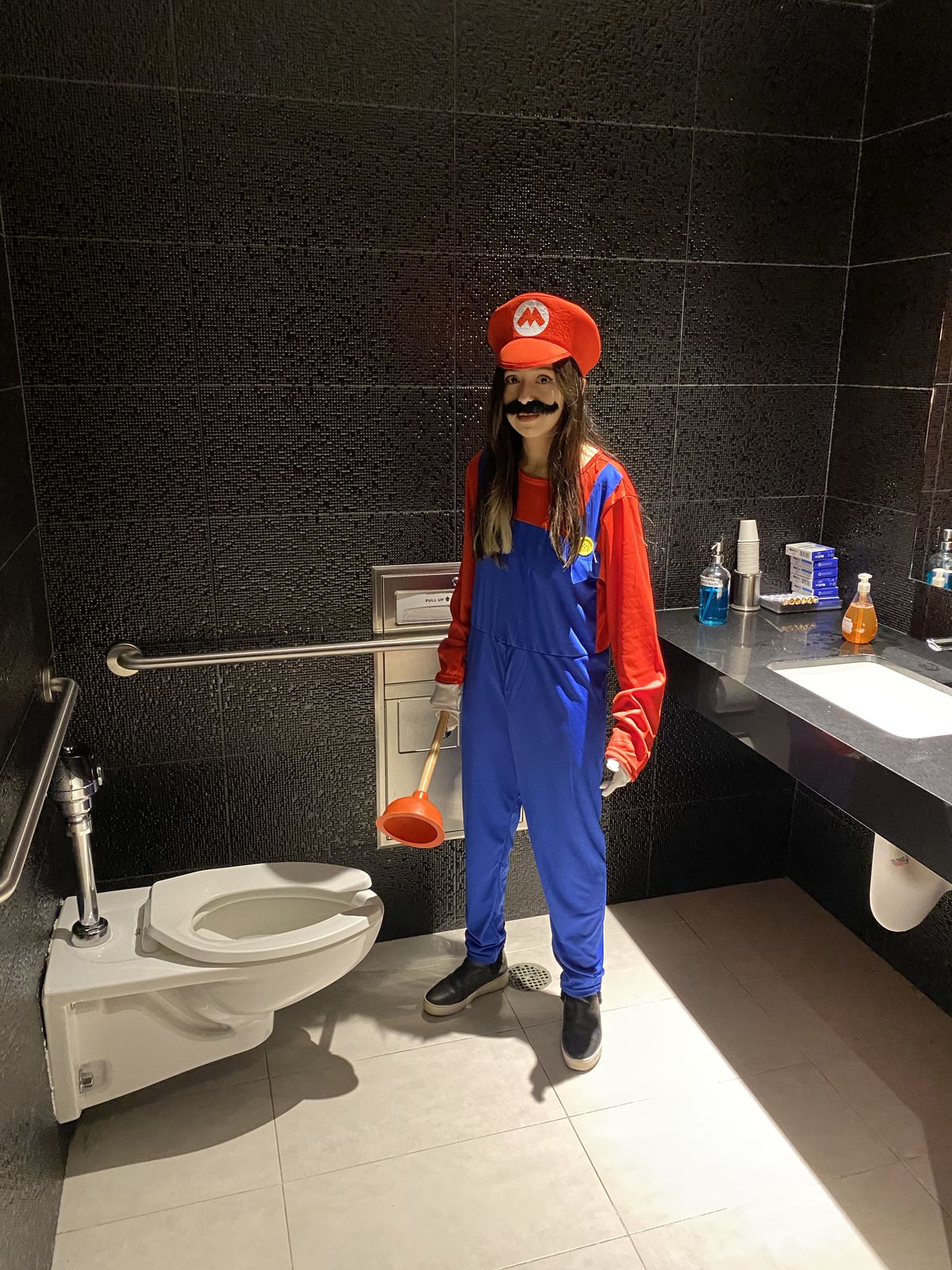 XTINA GG, déguisé en Mario, se tient dans une salle de bain tenant un piston au-dessus des toilettes.