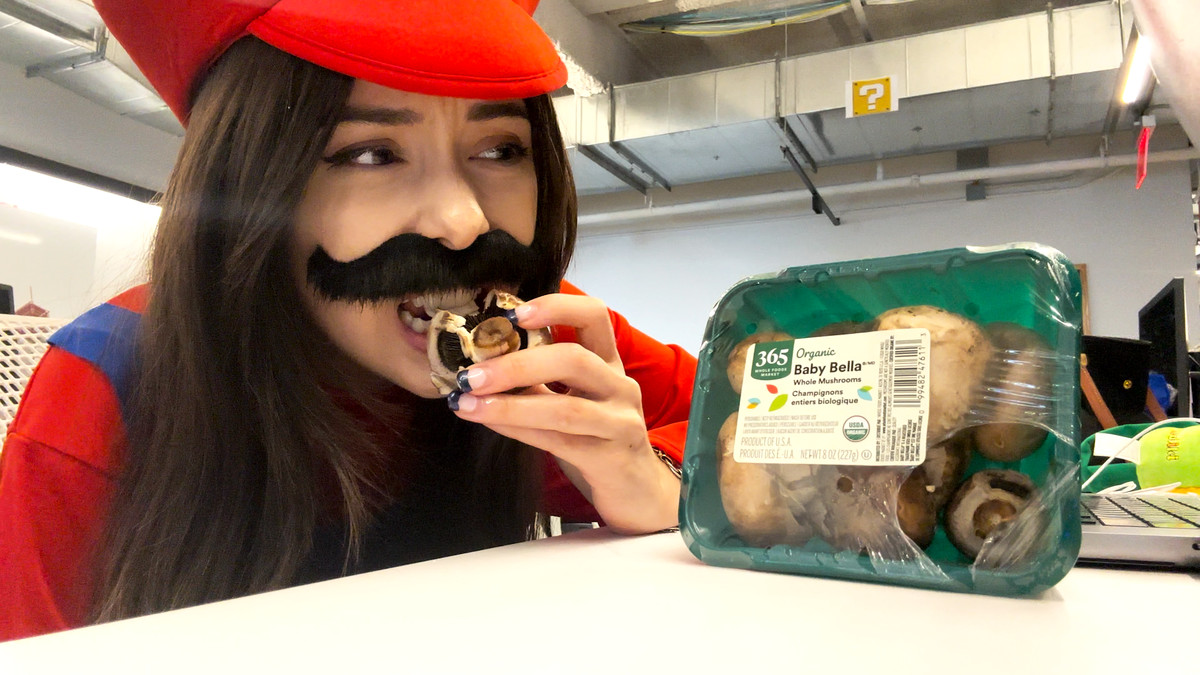Tina, déguisée en Mario, grimaçant en mordant dans un champignon cru Baby Bella.