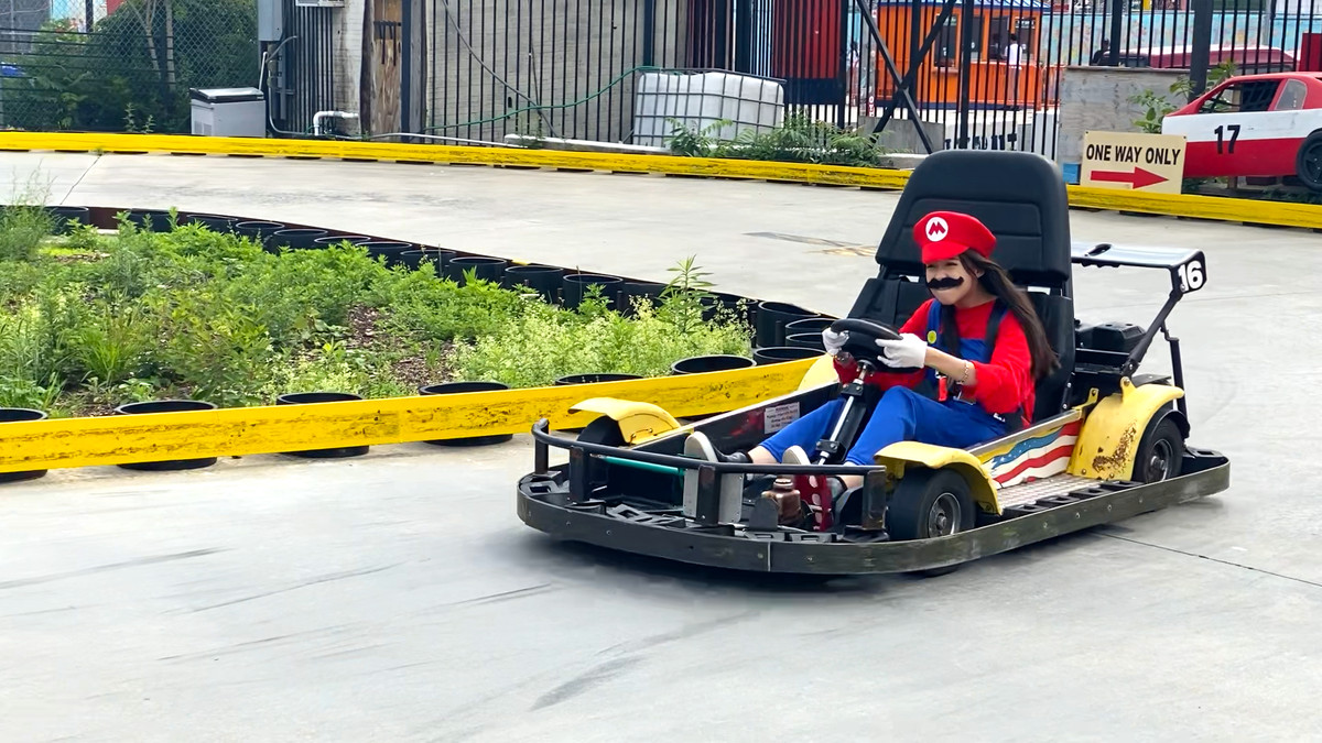 Tina déguisée en Mario, conduisant un kart, un regard d'intense concentration sur le visage.