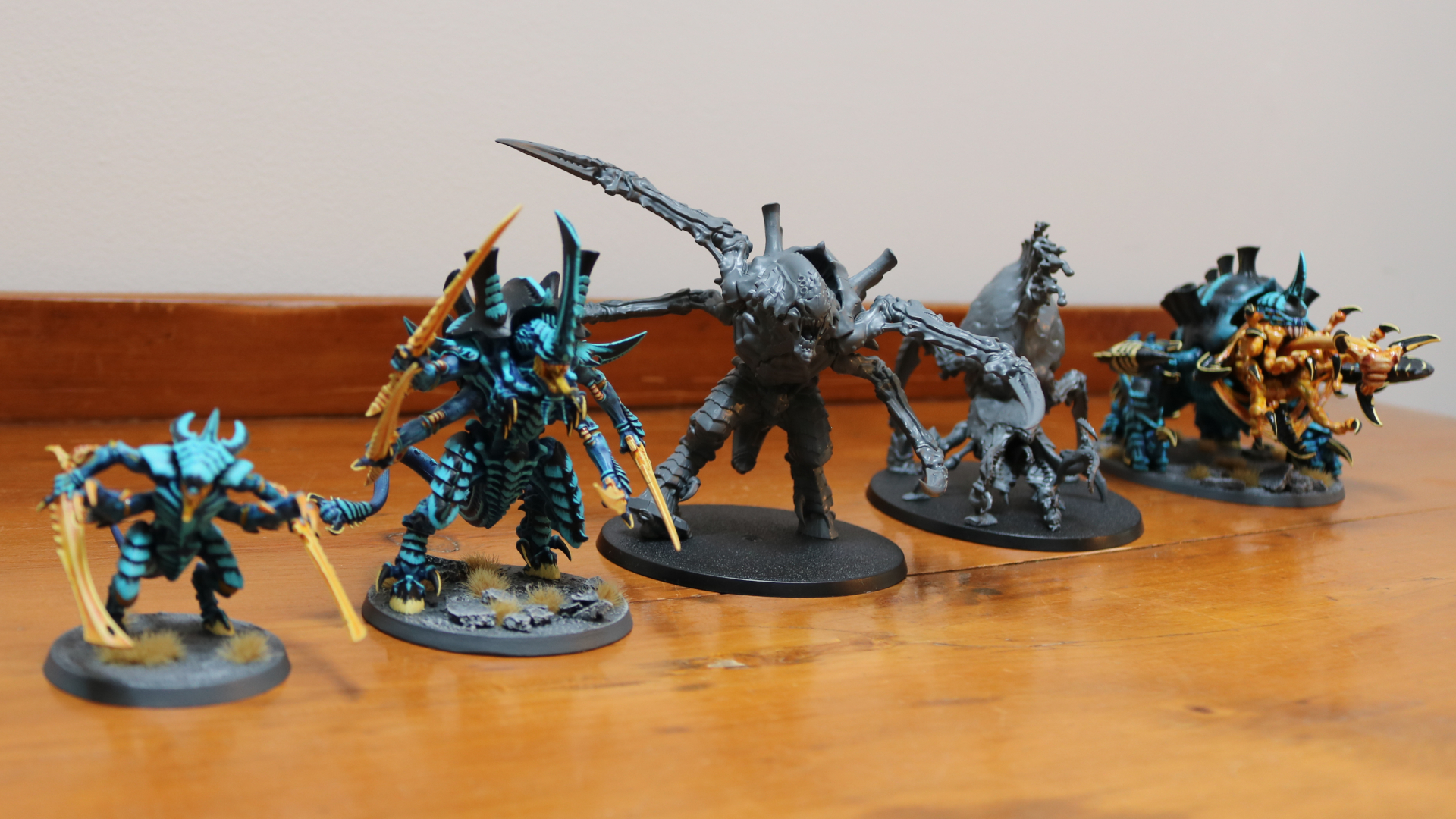 Une sélection de nouvelles et anciennes figurines Warhammer 40 000 Tyranid disposées en rang sur une table en bois