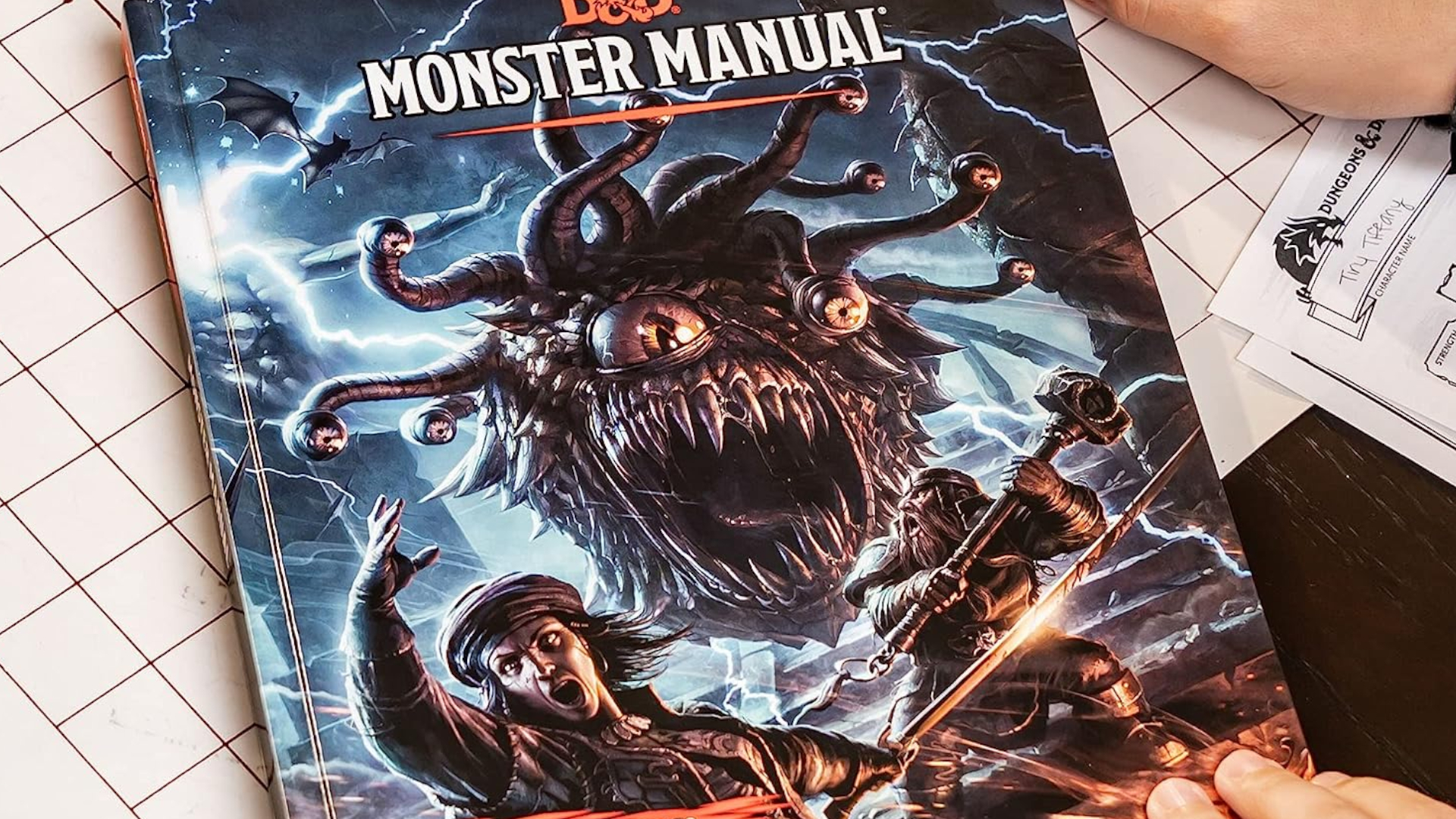 Livre Monster Manual tenu au-dessus d'une table et d'une grille