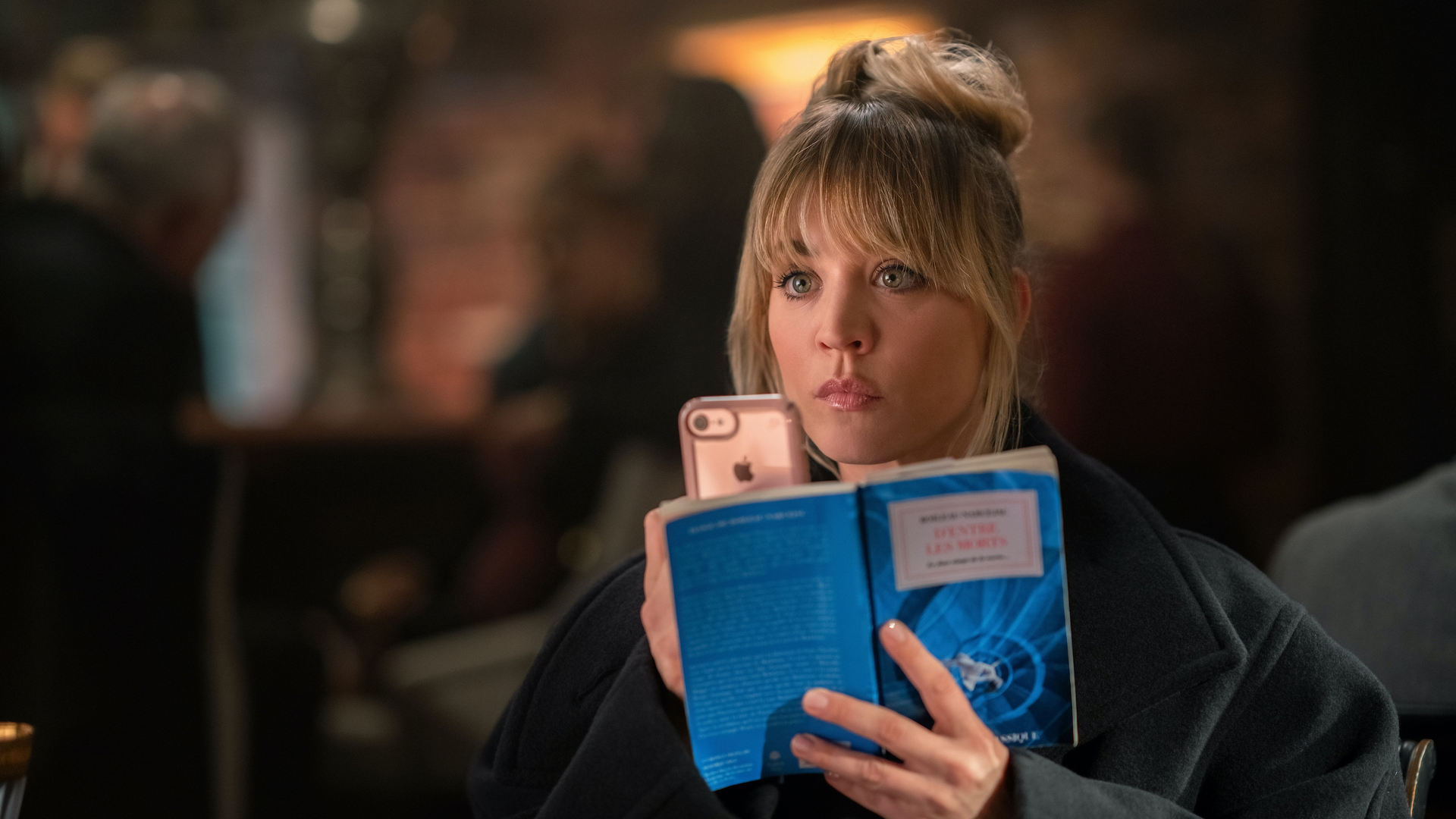 Kaley Cuoco dans le rôle de Cassie Bowden, tenant un téléphone et un roman dans The Flight Attendant Saison 2 Episode 1