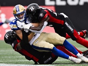 Le receveur éloigné des Blue Bombers de Winnipeg Drew Wolitarsky est plaqué par le demi défensif du Rouge et Noir d'Ottawa Damon Webb (à gauche) et le demi défensif Brandin Dandridge samedi à Ottawa.  Justing Tang / La Presse Canadienne