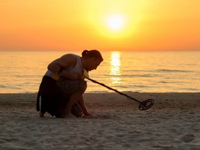 L'homme utilise un détecteur de métaux sur la plage au coucher du soleil