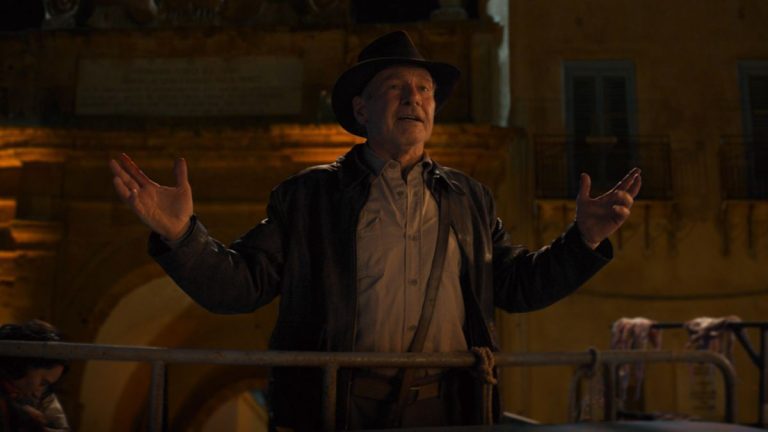 Harrison Ford gesturing with his arms as he speaks in a nighttime scene in Indiana Jones and the Dial of Destiny.