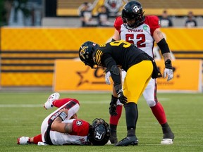 L'ailier défensif des Tiger-Cats Mason Bennett (90) et le joueur de ligne offensive des Redblacks Zack Pelehos (52) vérifient le quart-arrière Jeremiah Masoli après qu'il a été blessé lors d'un jeu dans la première moitié du match de samedi à Hamilton.