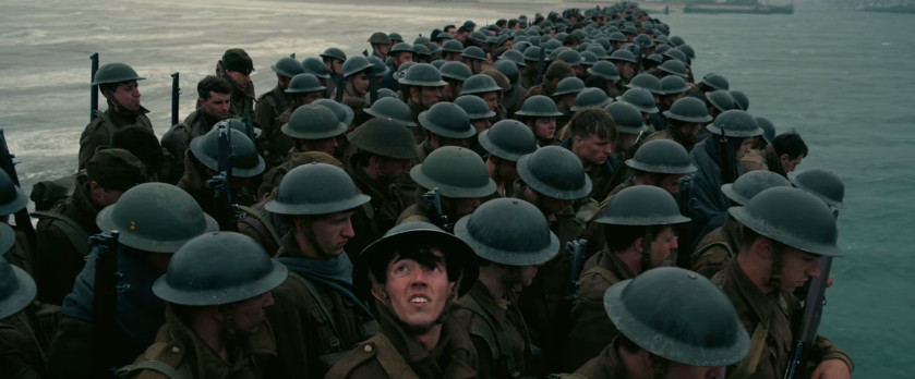 Un soldat regarde vers le haut à bord d'un bateau d'évacuation rempli d'autres soldats portant des uniformes identiques et des casques ronds en métal à Dunkerque. 