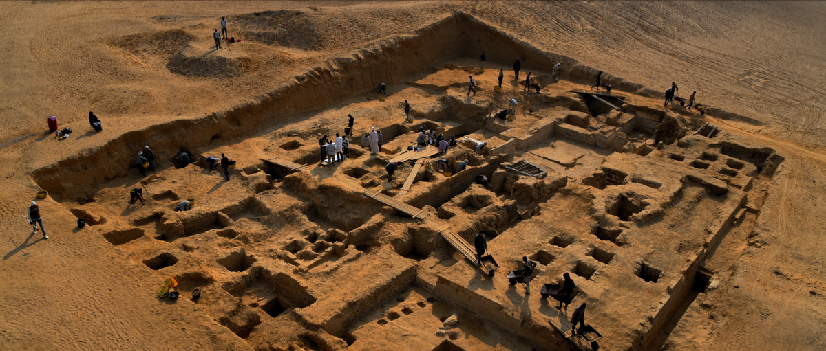 Un plan large d'un ensemble de ruines dans le sol, avec des gens qui y travaillent