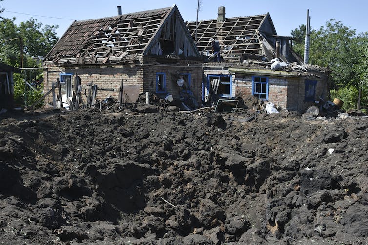 Un grand cratère de terre et de gravats à côté de maisons endommagées.