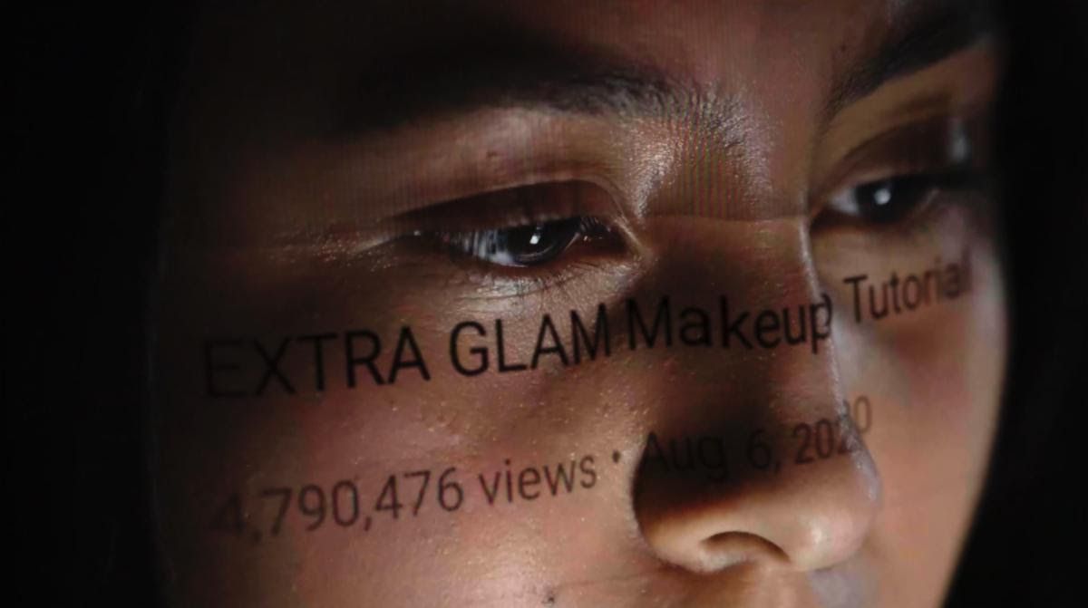 Le visage d'un jeune comme les mots « EXTRA GLAM MAKEUP Tutorial;  4 790 476 vues ;  2020 » jouent sur leur visage comme un reflet de l'écran.