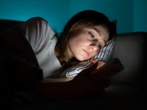 Femme utilisant un téléphone portable en position couchée dans son lit la nuit, souffrant d'insomnie post-rupture.  Anxiété.