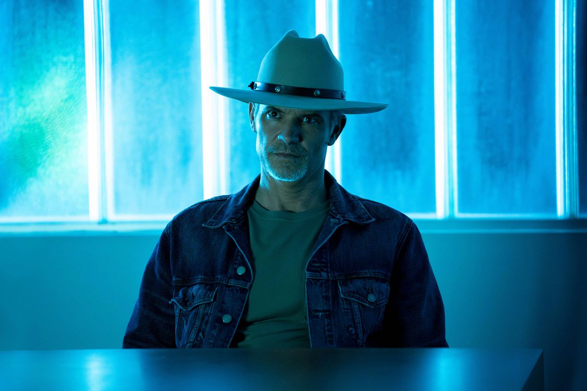 Raylan Givens (Timothy Olyphant) assis devant un néon, l'air énervé