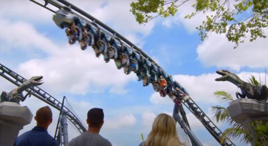 Guests walking under the track and in-between two Raptor statues at the Jurassic World VelociCoaster.