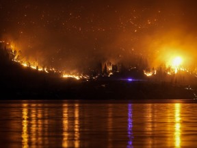 Le feu de forêt de McDougall Creek brûle à flanc de montagne au-dessus des maisons au bord du lac, à West Kelowna, en Colombie-Britannique, le vendredi 18 août 2023.