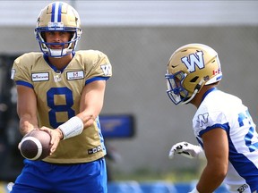 Le quart-arrière Zach Collaros (à gauche) tient le ballon au porteur de ballon Brady Oliveira lors de l'entraînement des Blue Bombers de Winnipeg, le lundi 7 août 2023.