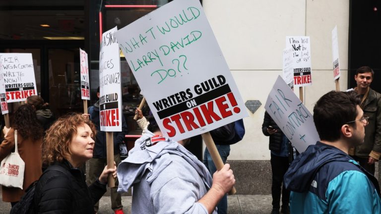 NEW YORK, NEW YORK - MAY 02: Members of the Writers Guild of America (WGA) East hold signs as they walk on the picket-line outside of the Peacock NewFront on May 02, 2023 in New York City. WGA members were out on the first day of a Hollywood voters strike after the board of directors for the Writers Guild of America, which includes West Coast and East Coast branches, voted unanimously to call for a walkout. Negotiations between a top guild and a trade association that represents Hollywood’s top studios failed to avert the first walkout in more than 15 years. Union members have stated that they are not being paid fairly in the streaming era and are seeking pay increases and structural changes to the business model. (Photo by Michael M. Santiago/Getty Images)