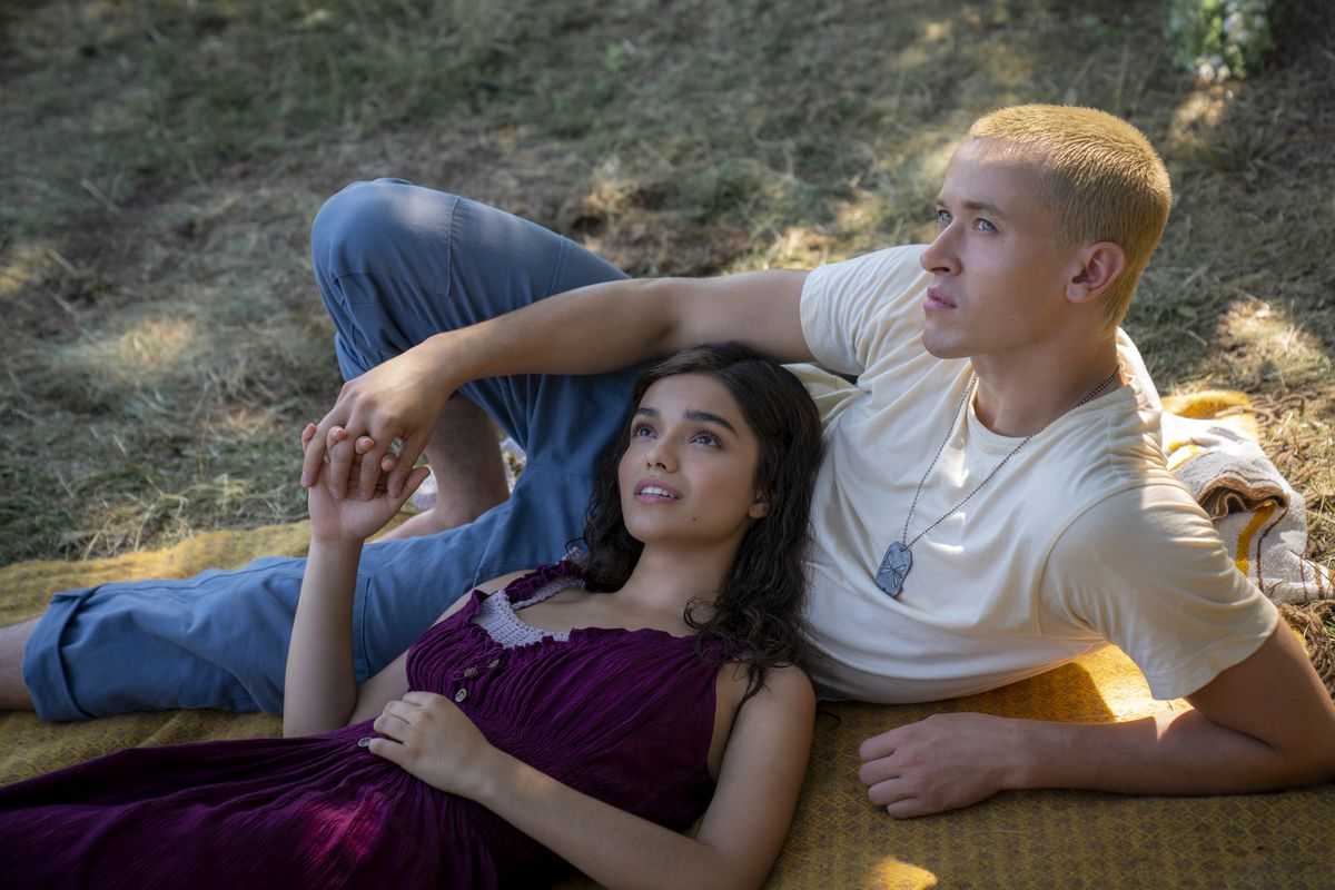 Rachel Zegler dans le rôle de Lucy Gray Baird dans une robe violette pose avec Tom Blyth dans le rôle de Coriolanus Snow qui porte un t-shirt blanc et des cheveux blonds décolorés dans The Hunger Games : La Ballade des oiseaux chanteurs et des serpents