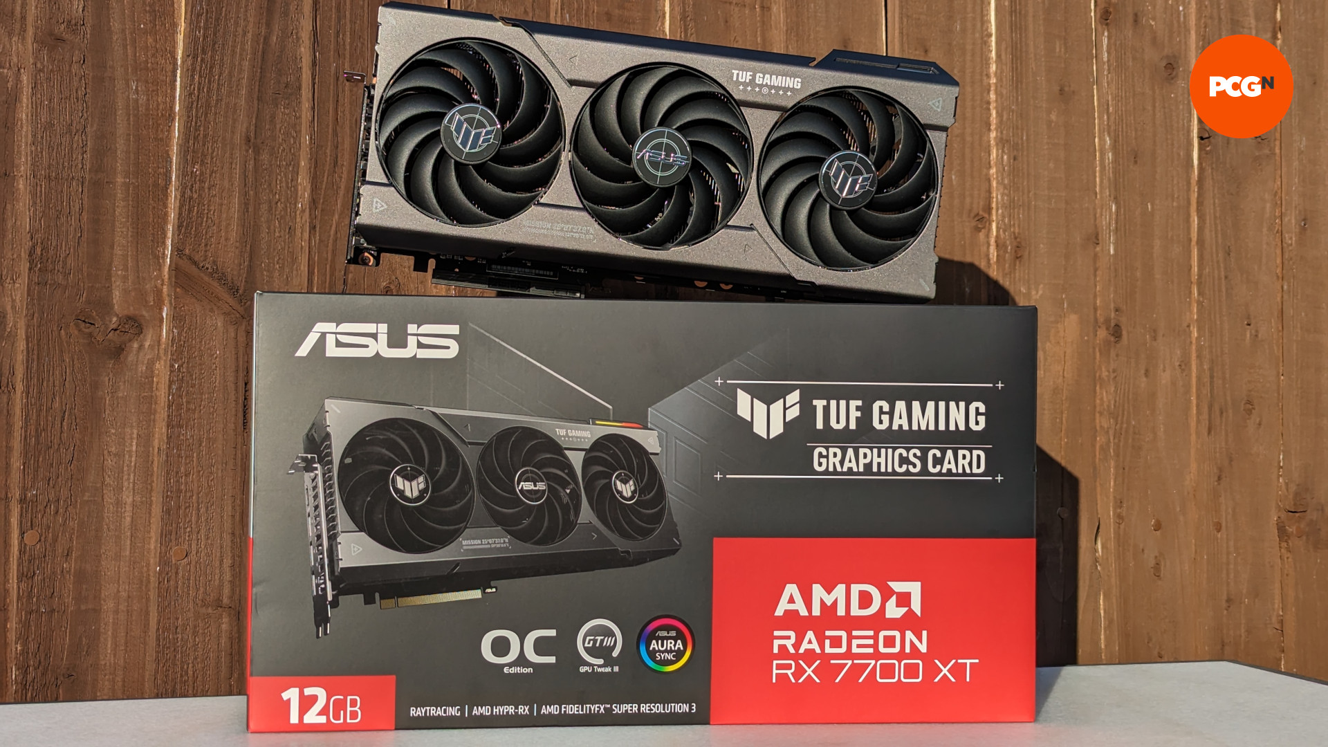 Test AMD Radeon RX 7700 XT : Le modèle ASUS TUF Gaming de la carte graphique, reposant sur son emballage de vente au détail avec un fond en bois