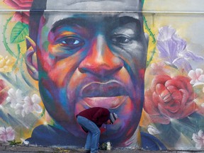 Un homme dépose des fleurs sur une fresque représentant George Floyd