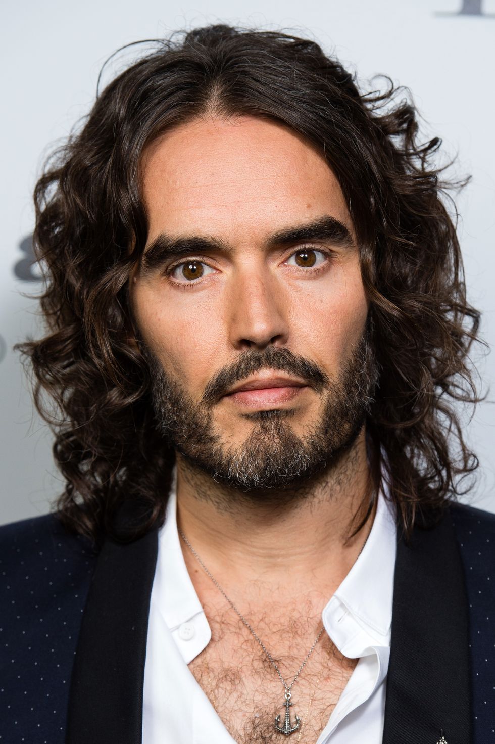 Russell Brand photographié en 2017, il a les cheveux longs et une barbe et regarde la caméra