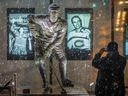 Un homme prend une photo d'une statue illuminée de la légende des Canadiens Jean Béliveau à l'extérieur du Centre Bell à Montréal le 3 décembre 2014, au lendemain du décès du Temple de la renommée à l'âge de 83 ans.