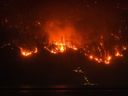 L'incendie de forêt de McDougall Creek brûle à flanc de montagne au-dessus d'une maison au bord d'un lac, à West Kelowna, en Colombie-Britannique, le vendredi 18 août 2023.