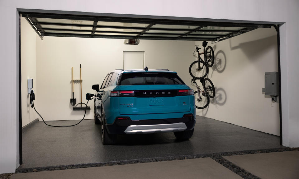 Photo marketing Honda du SUV électrique Prologue en charge dans un garage domestique.  Deux vélos sont suspendus sur des supports muraux à droite du véhicule.