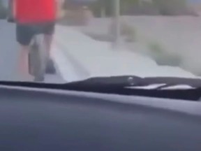 Capture d'écran d'une vidéo prise par un passager d'une voiture circulant derrière un cycliste en chemise rouge.