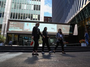 Des piétons passent devant un panneau d'affichage du TSX dans le quartier financier de Toronto.  Certains Canadiens ont mis leurs projets d'investissement sur la glace en raison de l'incertitude économique, selon un sondage.