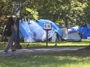 Une personne traverse l'immense campement de sans-abri d'Allan Gardens à Toronto avec trop de tentes et de structures pour pouvoir compter le mardi 22 août 2023.