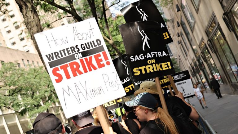 NEW YORK, NEW YORK - JULY 20: Members of the Writers Guild of America and SAG-AFTRA hold up signs outside of 30 Rockefeller Plaza on July 20, 2023 in New York City. Members of SAG-AFTRA, Hollywood's largest union which represents actors and other media professionals, have joined striking WGA (Writers Guild of America) workers in the first joint walkout against the studios since 1960. The strike could shut down Hollywood productions completely with writers in the third month of their strike against the Hollywood studios.  (Photo by Cindy Ord/Getty Images)